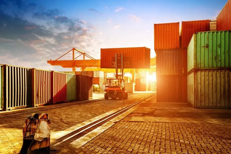 Shipping containers stacked at a port with a forklift operating between rows