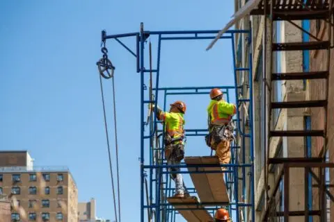 Two construction workers wearing safety harnesses standing on metal scaffolding