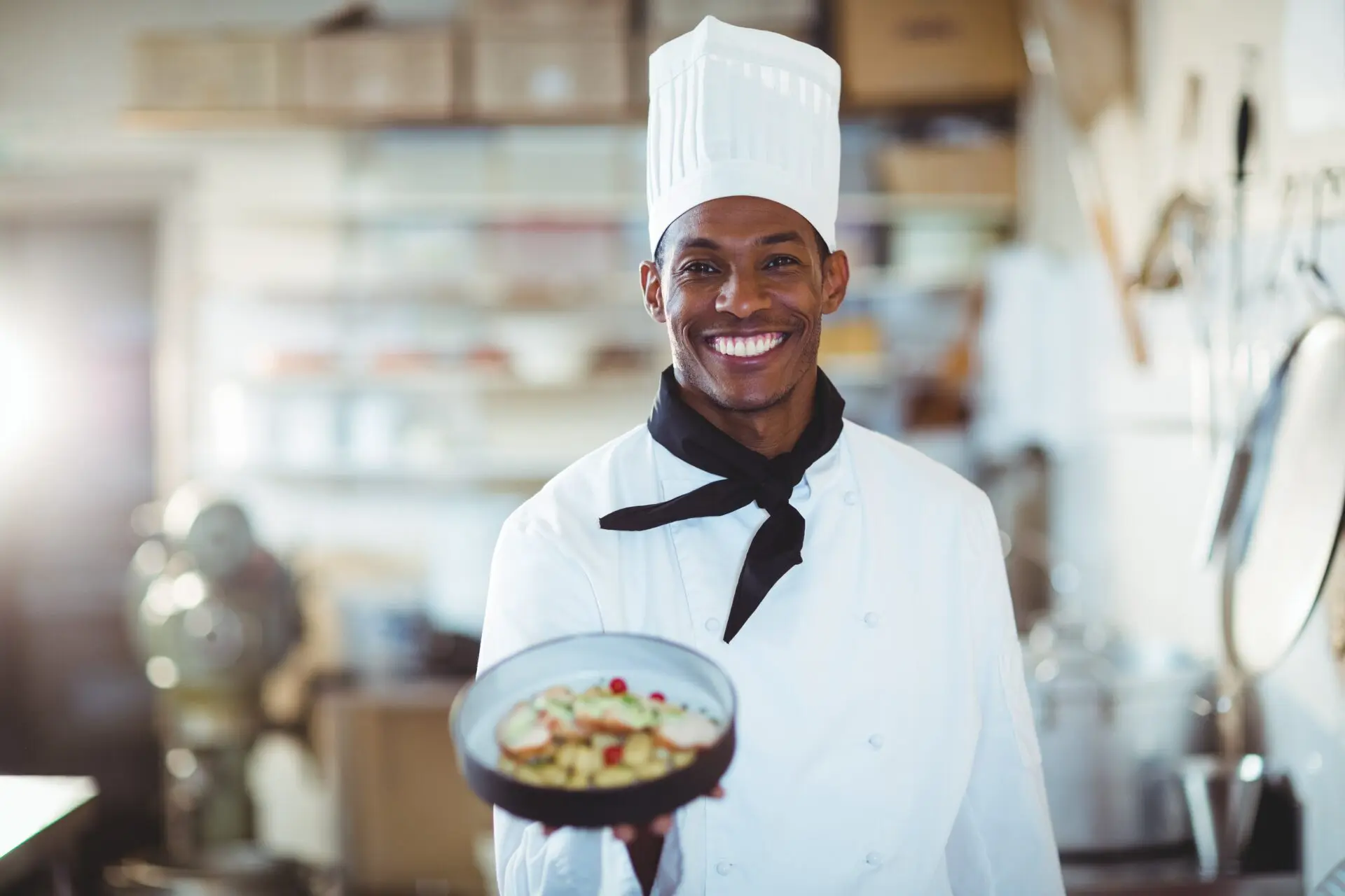 Chef smiling while holding a prepared dish inside a professional kitchen