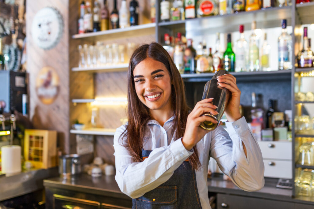 Bartender smiling while shaking a cocktail behind a bar