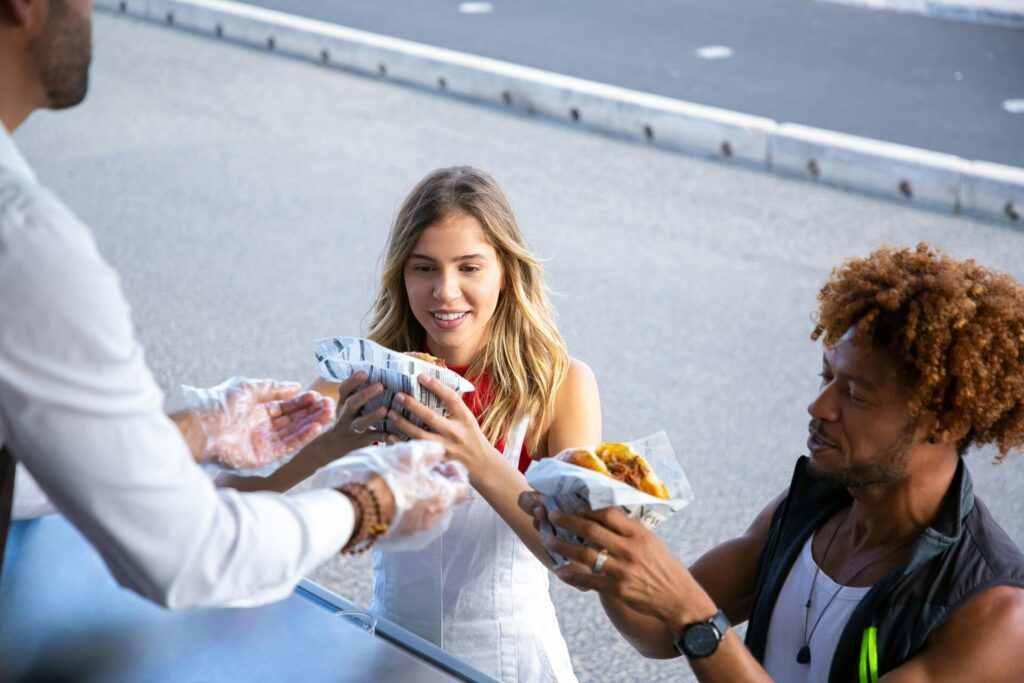 Street food vendor handing wrapped food to two customers at a food truck