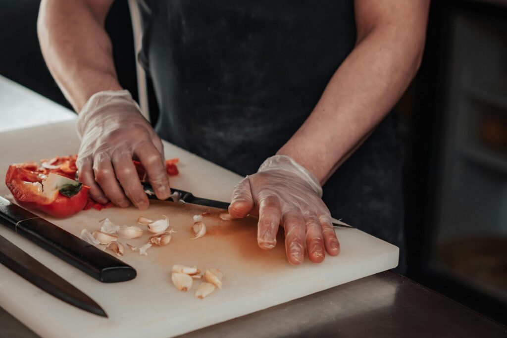 Cook wearing gloves slicing vegetables on a cutting board in a kitchen
