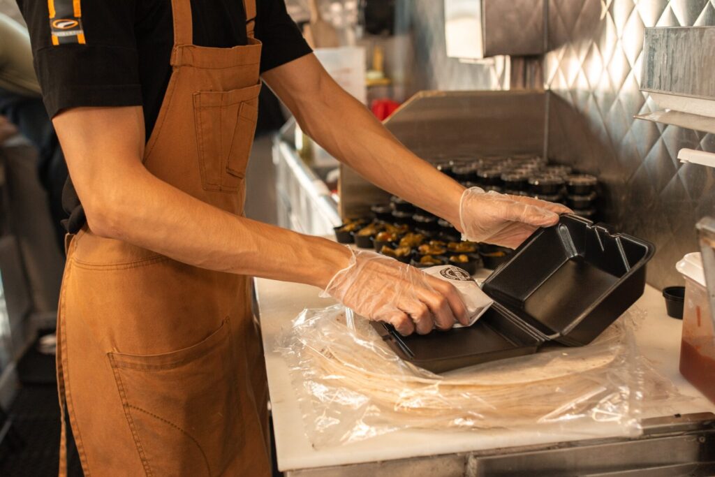 Food worker packing a meal into a takeaway container in a commercial kitchen