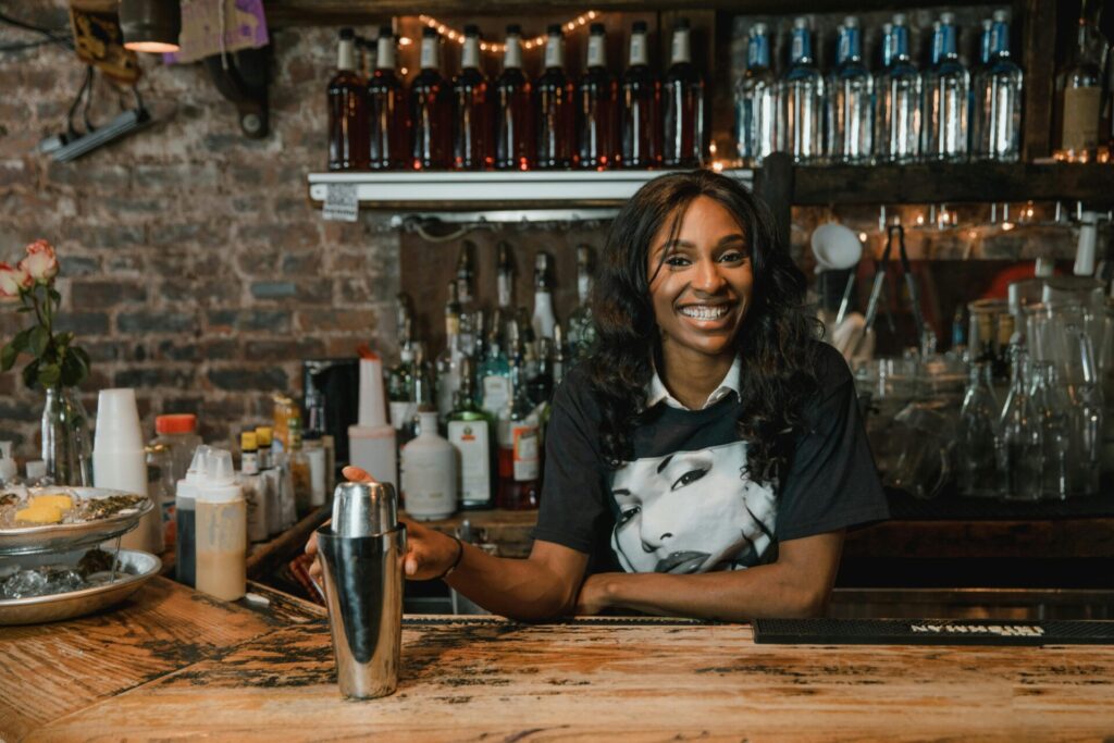 Bartender smiling behind a bar while holding a cocktail shaker