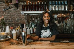 Bartender smiling behind a bar while holding a cocktail shaker